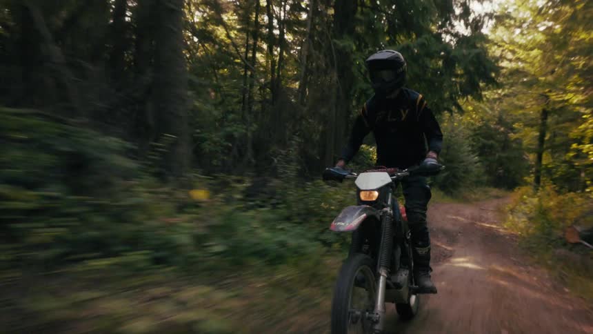 Motocross rider riding along a dirt trail in a forested area with motion blur