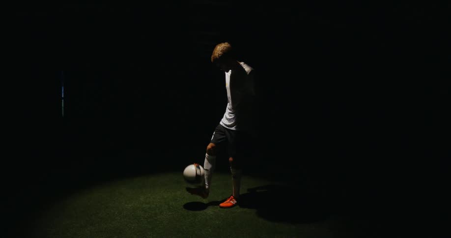 Person dribbles a ball off their foot at night