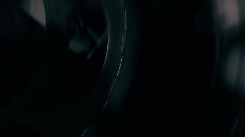 A close view of a large black film reel spinning slowly in a dark room with subtle highlights on its metallic surface