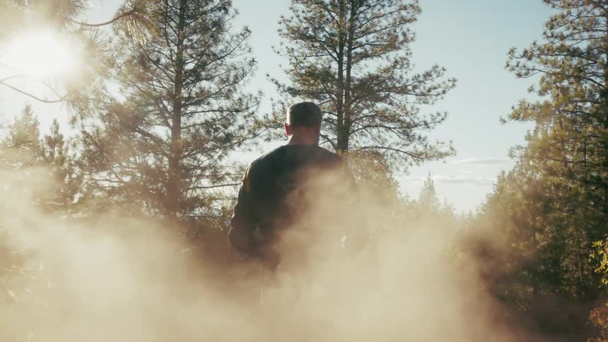 Rider adjusting helmet in a forested area with dust suspended and lit by sunlight