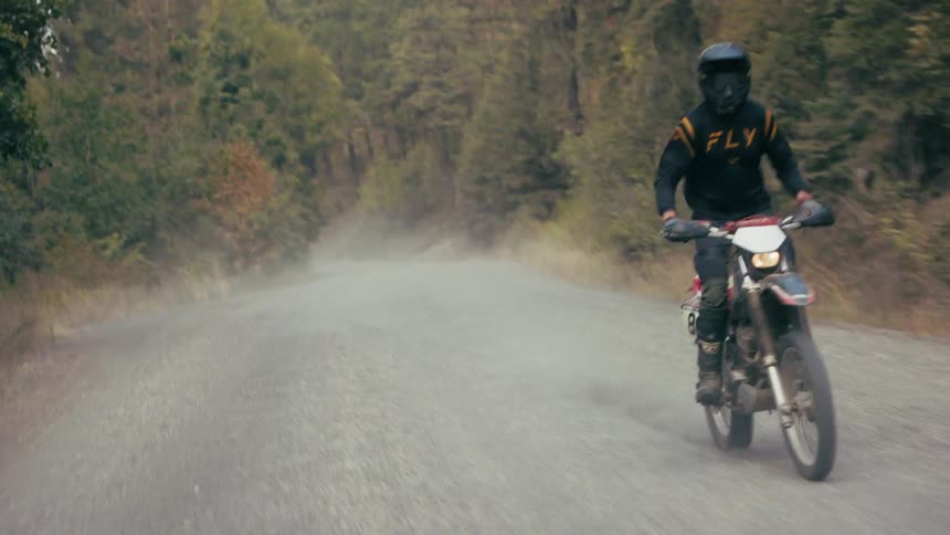 Motorcyclist speeds on gravel road surrounded by dense forest