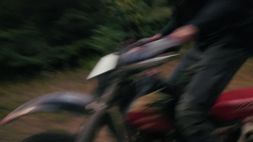 Motorcyclist rides a motorcycle along a path through the woods during the daytime