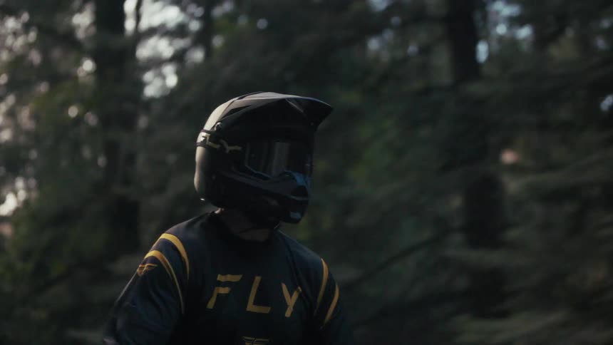 Black helmet with reflective visor and dark outfit with yellow accents in wooded area