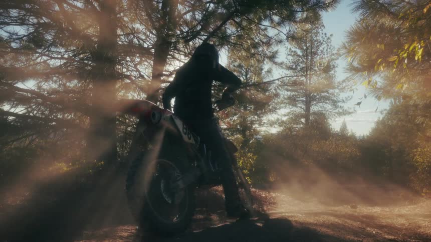 A rider in a helmet approaches their dirt bike on a dusty forest trail as the sun shines brightly through the treesthe figure mounts the motorcycle and prepares to ride while surrounded by golden light and hazy dust