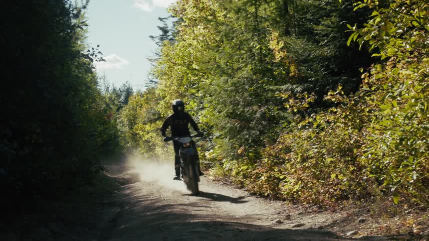 Cyclist riding a motorbike on a dirt road through the woods