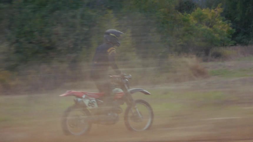 A motorcyclist rides off road across an open dirt field on a motocross adventure