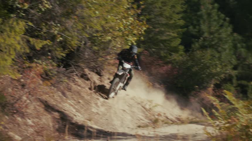 Dirt bike rider speeds down a rugged slope kicking up dirt along the forest trail