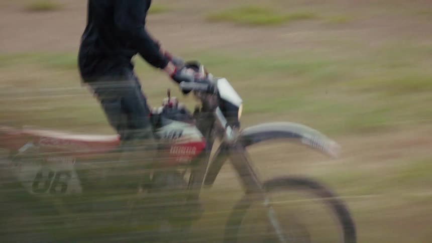 A rider wearing a black fly racing helmet and gear speeds across a grassy field on a red and white honda dirt bike numbered 86 the footage uses a panning motion with a slow shutter effect creating a sense of rapid movement through the blurred background