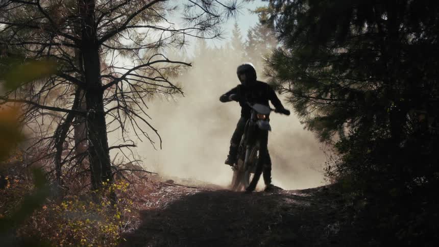 The man races his dirt bike around the dirt trail in the dense forest