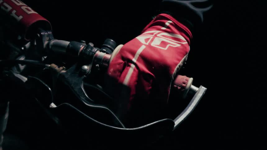 Gloved hand gripping a motorcycle handlebar and lever in a dark setting