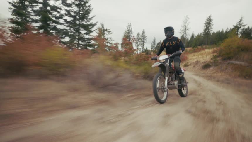 Biker wearing a helmet riding a motorcycle over a dust road on a mountain with trees and vegetation to the sides outdoors during day time