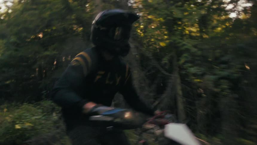 A motorcycle rider races swiftly along a winding forest trail on a dirt bike