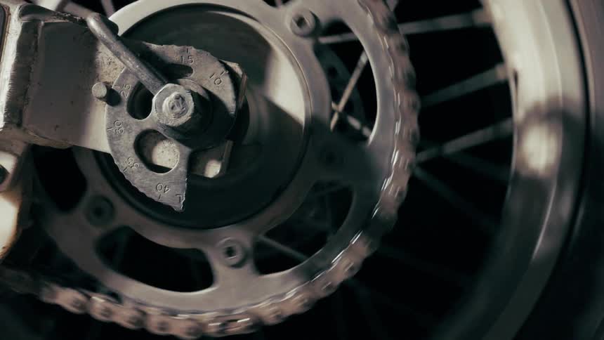 A closeup shot captures a motorcycles rear sprocket and chain coming to a complete stop as the wheel ceases to spinthe mechanical details of the drive system are visible showing the metal chain settling into the teeth of the sprocket against a dark