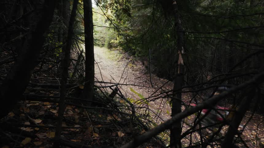 Motocross rider traveling along a narrow trail in a forested area seen through trees