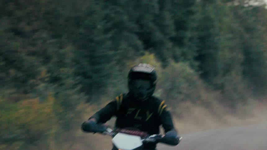 Motorcyclist rides forest trail wearing black outfit with yellow logo
