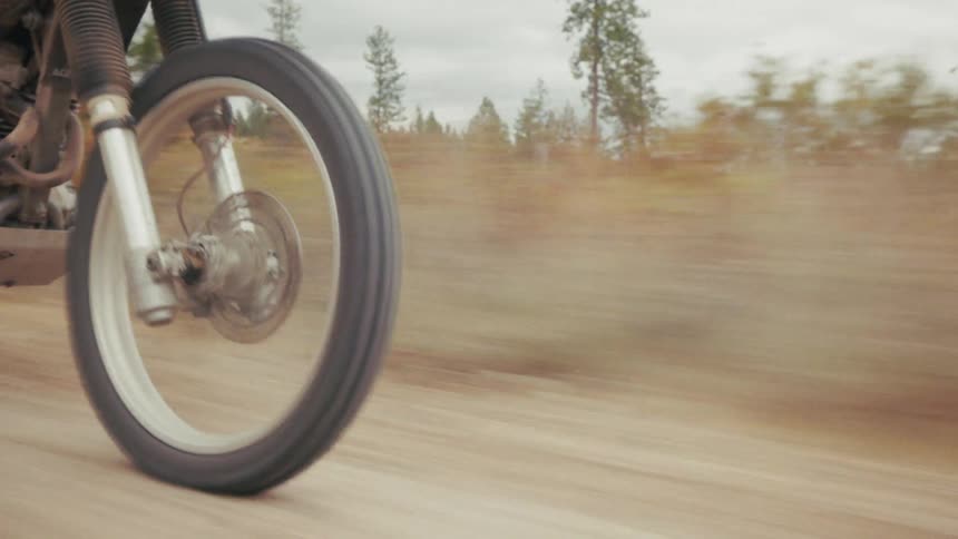 Motorcycle in motion kicks up dust on dirt road surrounded by vegetation