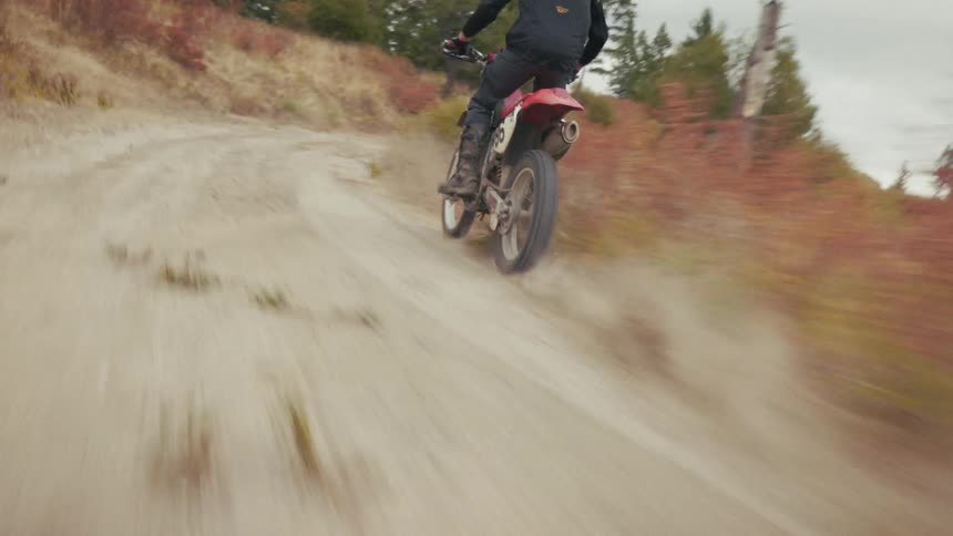 Motocross rider moving away on a dirt trail with dust rising in an open area