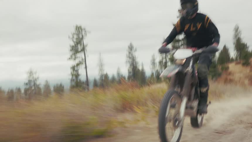 Motocross rider riding on a dirt trail with dust rising in a wooded mountainous area