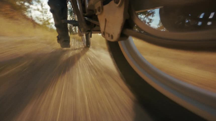 Motorcycle wheel kicks up dust on sunlit dirt trail