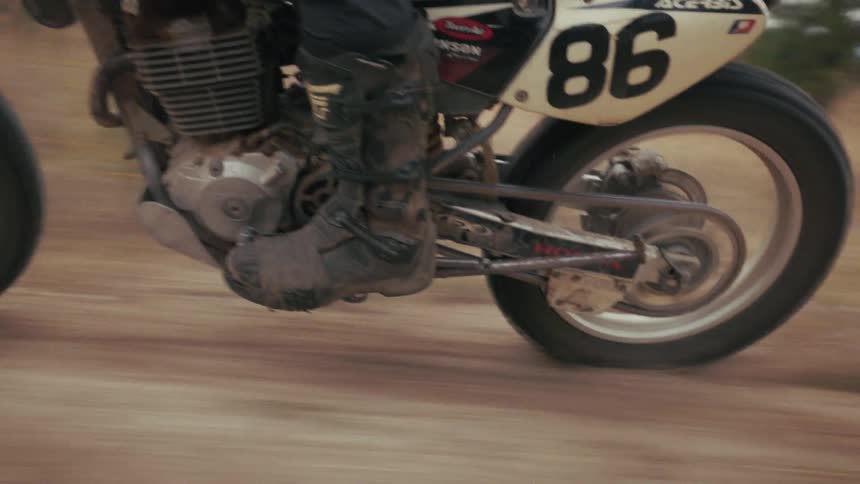 A red and black honda dirt bike speeds across a dusty trail its wheels spinning rapidly as the rider navigates the uneven terrainthe camera tracks the lower half of the motorcycle highlighting the mudcaked boots of the rider and the mechanical move