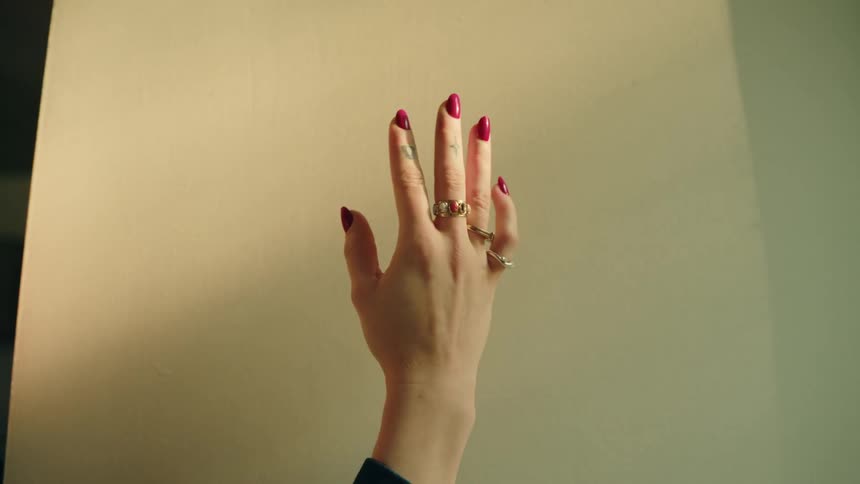 A hand with red nail polish and rings is modeling in front of a light background that shows shadows