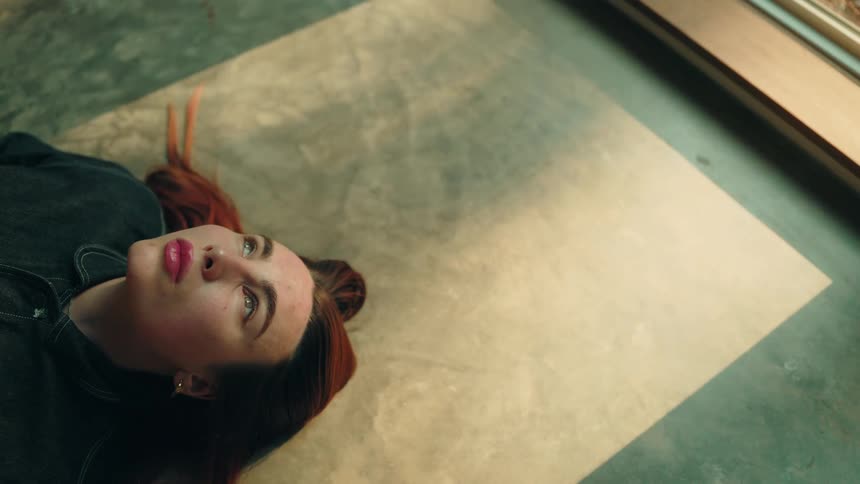Young adult woman wearing a denim shirt lying down on the floor indoors during day time