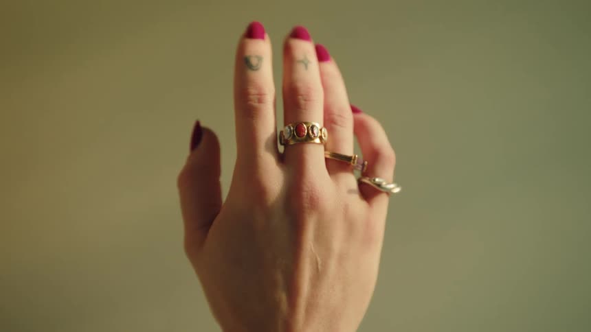 Hand with redpainted nails and metal rings resting against a smooth wall
