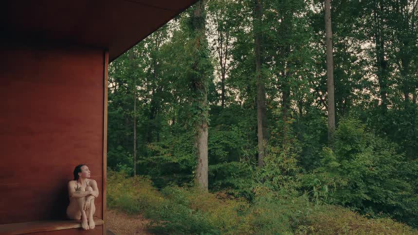 Woman sitting by a wooden structure observing the surrounding forest