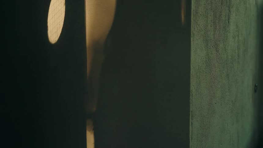 Shadow of a woman passes through a partially lit doorway indoors