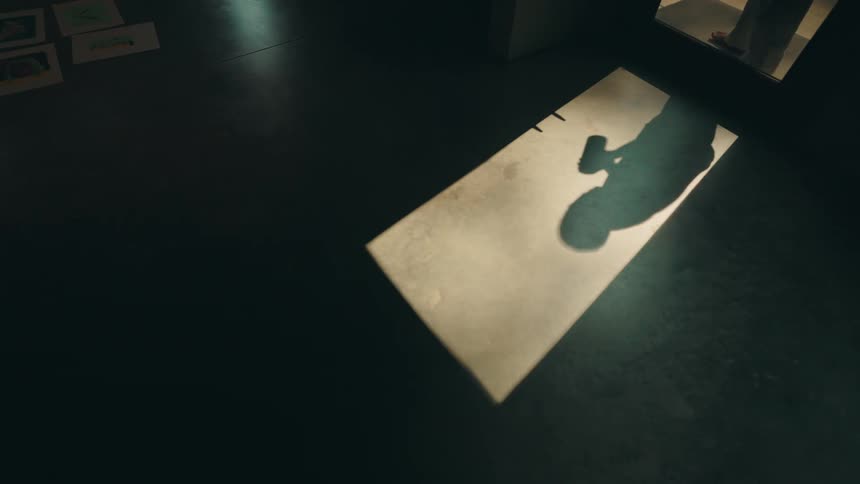 Shadow of a person having a beverage seen against the floor of a dark room indoors during night time