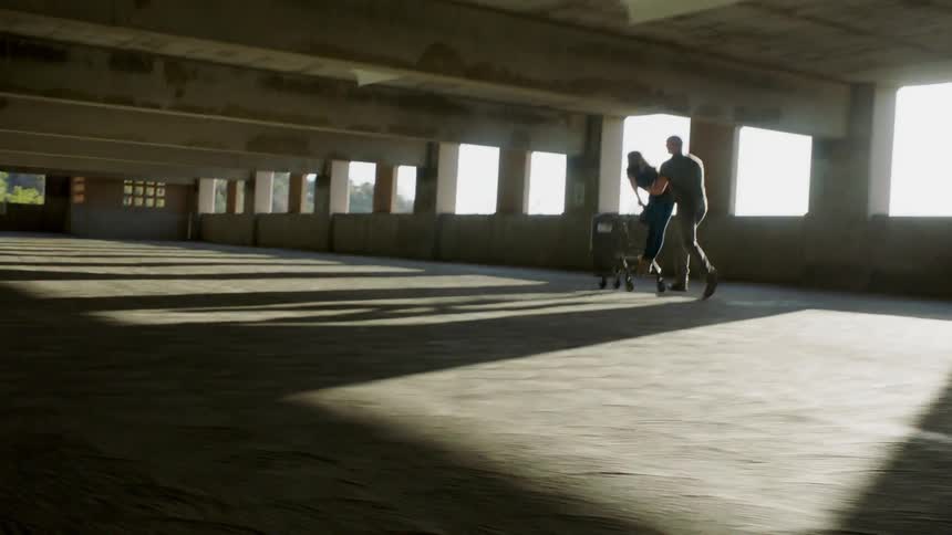 Man pushes a woman who is riding on a cart through an empty parking ramp
