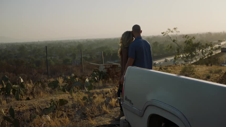 A man and woman hug atop a hill above a freeway