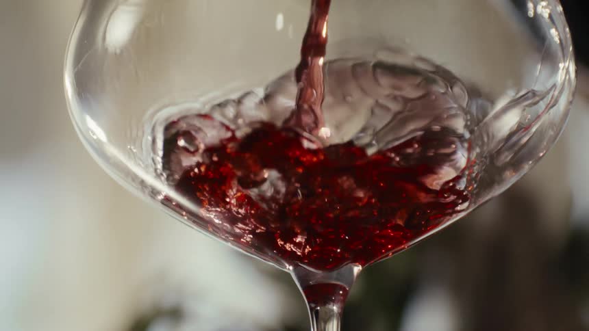 Red wine is being poured into a clear wine glass
