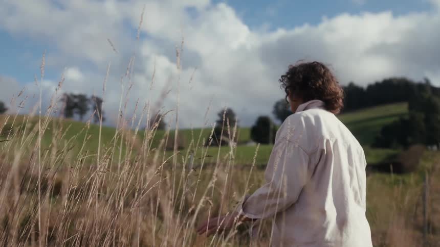 The woman is walking through the reeds on the field