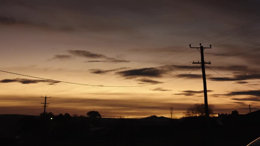 F a sunset or sunrise over a dark silhouetted landscape with hills in the distancepower lines and utility poles stand in the foreground against a sky filled with layers of orange and purple clouds