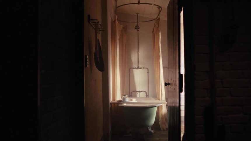 Freestanding bathtub set in a narrow bathroom with light curtains and natural light