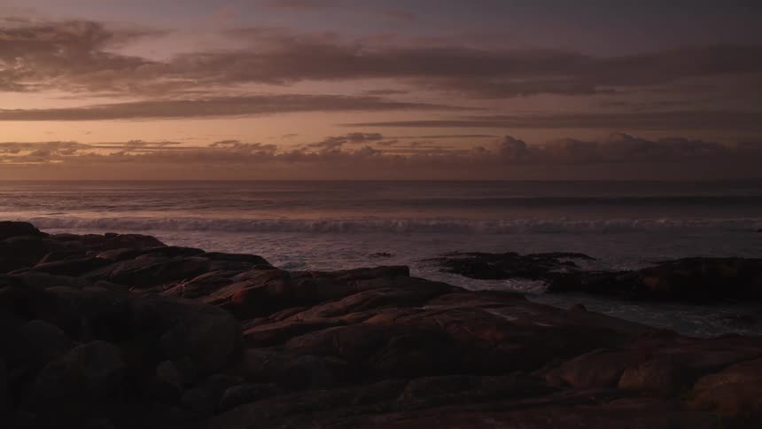 Calm ocean with colorful sunrise sky over dark rocks