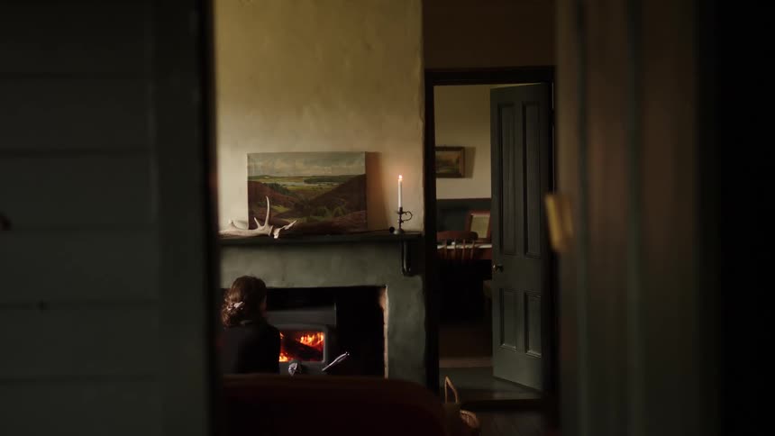 Person sitting by a lit fireplace in an indoor setting seen through a partially open doorway