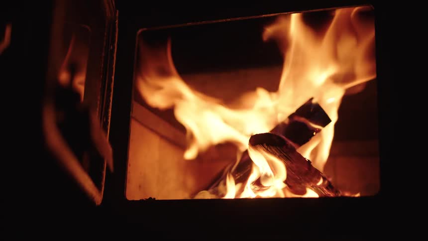 Bright orange flames flicker and rise from burning logs inside a dark wood burning stove