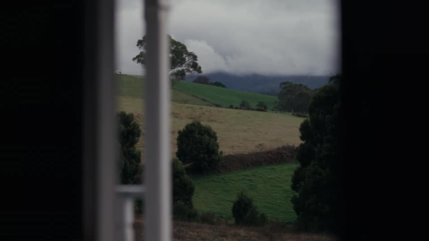 Rural landscape with green hills and trees seen through an opening with a cloudy sky in the background