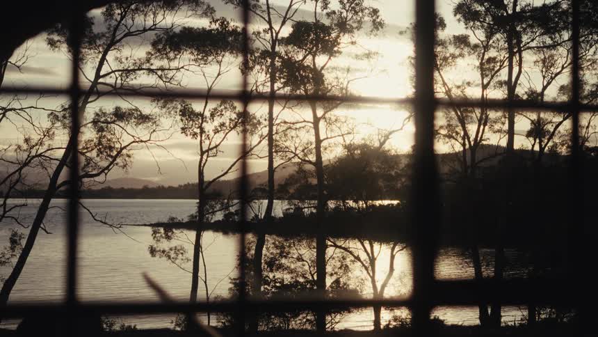 Window faces a lake scene with the sun casting mountains and trees into silhouette