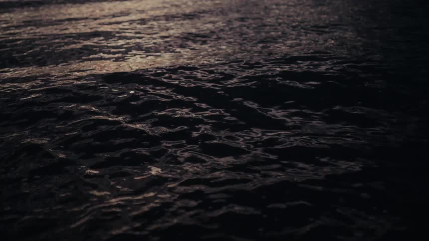 A close view of dark water with small ripples moving across the surface under a dim light