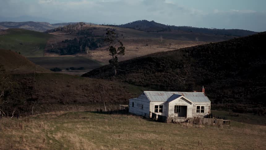 Isolated rural house in open fields with dry hills and sparse vegetation surrounding it