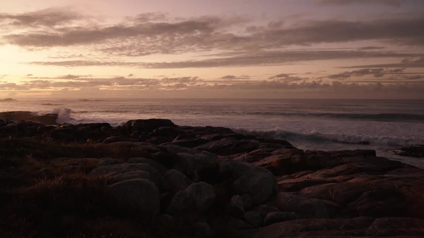 Rocky shoreline with gentle waves under a sunsetlit sky