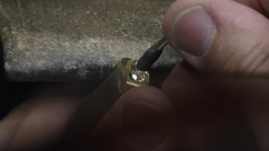 A jeweler uses a precision tool to carefully set a small gemstone into a metal mounting