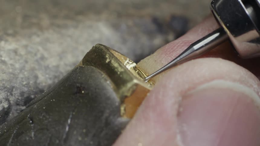 A jeweler uses a precision rotary tool to carefully carve and refine the interior setting of a gold ringgolden dust particles are visible as the metal is shaved away highlighting the intricate detail and steady hand required for highend jewelry fabri