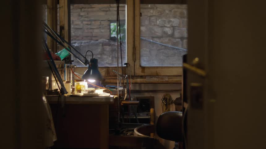 Craft workbench lit by a desk lamp in a workshop with tools and a window in the background