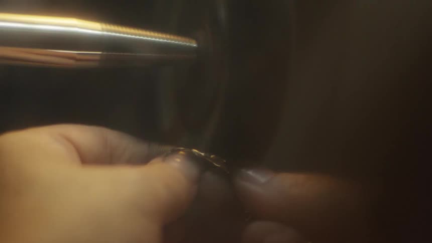 A jeweler uses a highspeed polishing wheel to buff a delicate gold chain their hands are darkened with polishing compound as they carefully work the metal against the rotating lathe