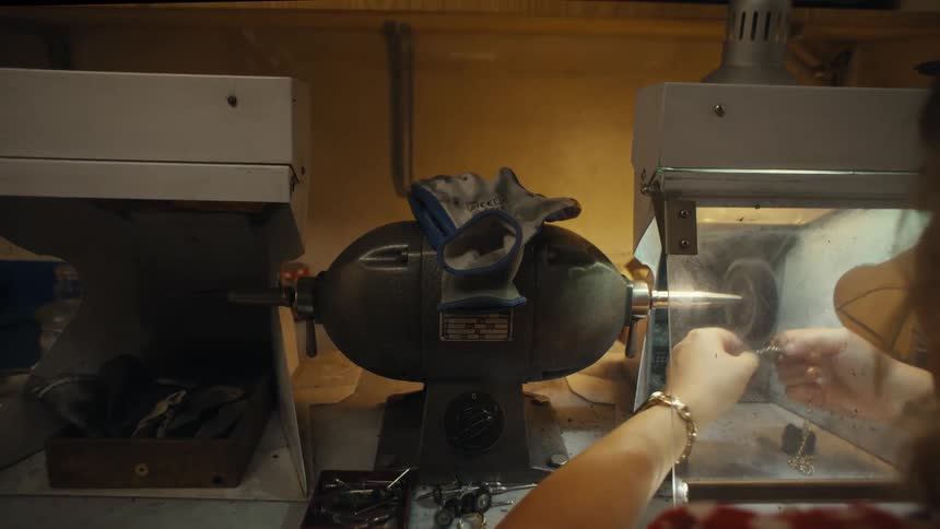 A jeweler polishes a gold chain on a spinning wheel in a workshop