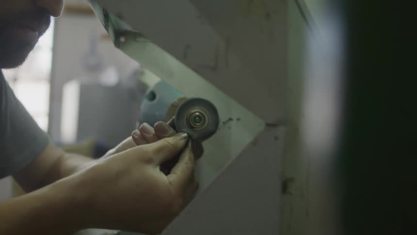 A close up side view shows a jeweler with a beard working in a shop using a small spinning polishing wheel to buff a piece of jewelry held in both hands